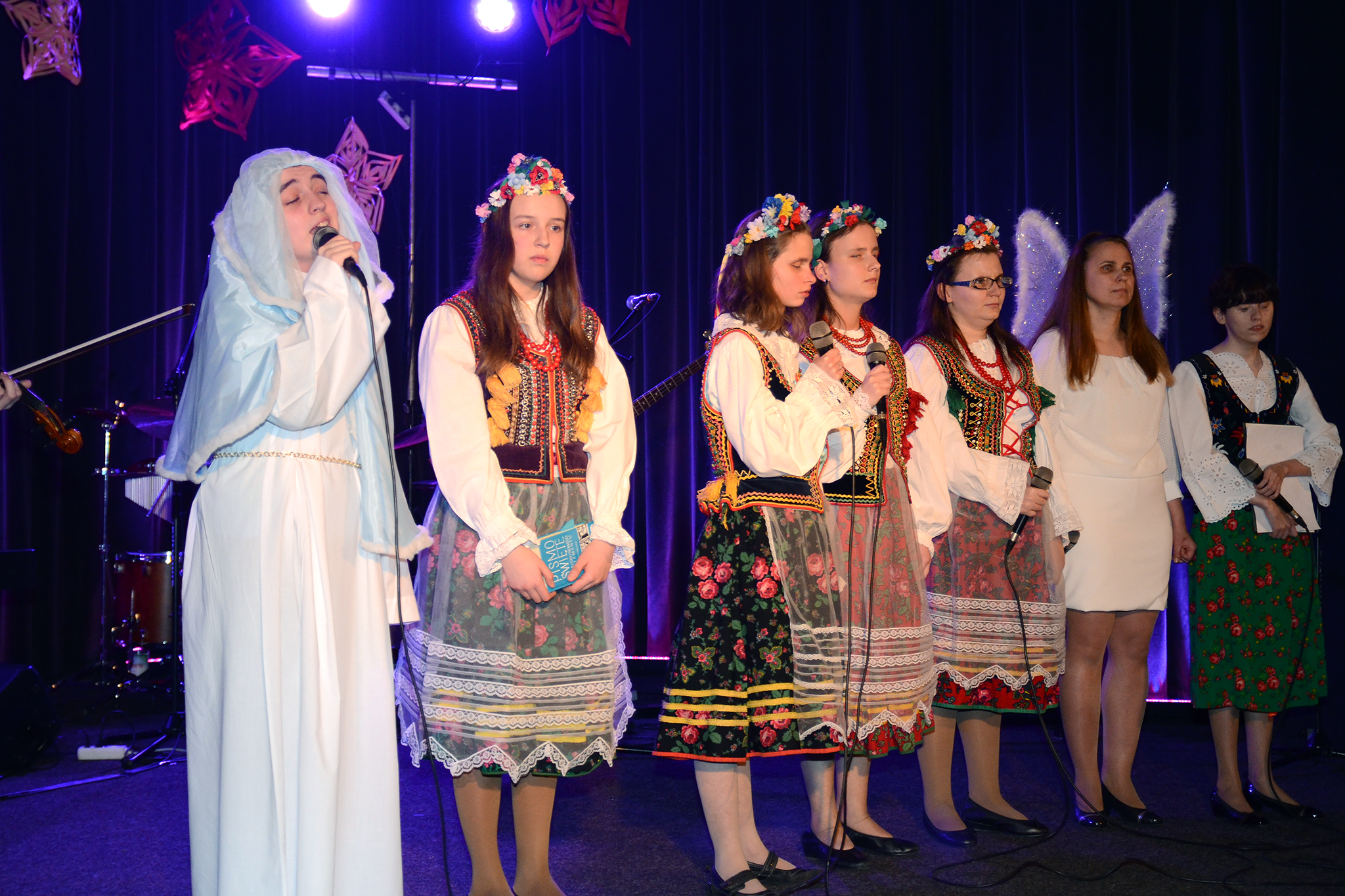 Śpiewająca Maryja. Obok niej stoi pięć dziewczyn w strojach krakowskich i Prezes Fundacji w stroju anioła